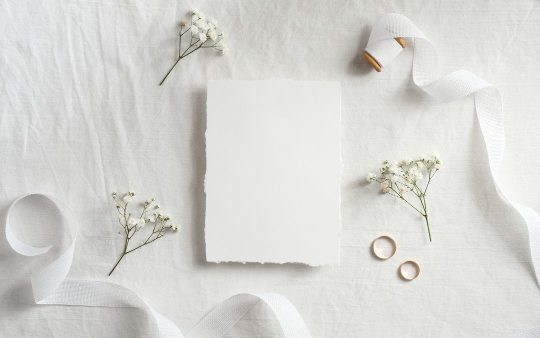 Wedding invitation card template. Top view blank paper card, ribbon, golden rings, flowers on white background.
